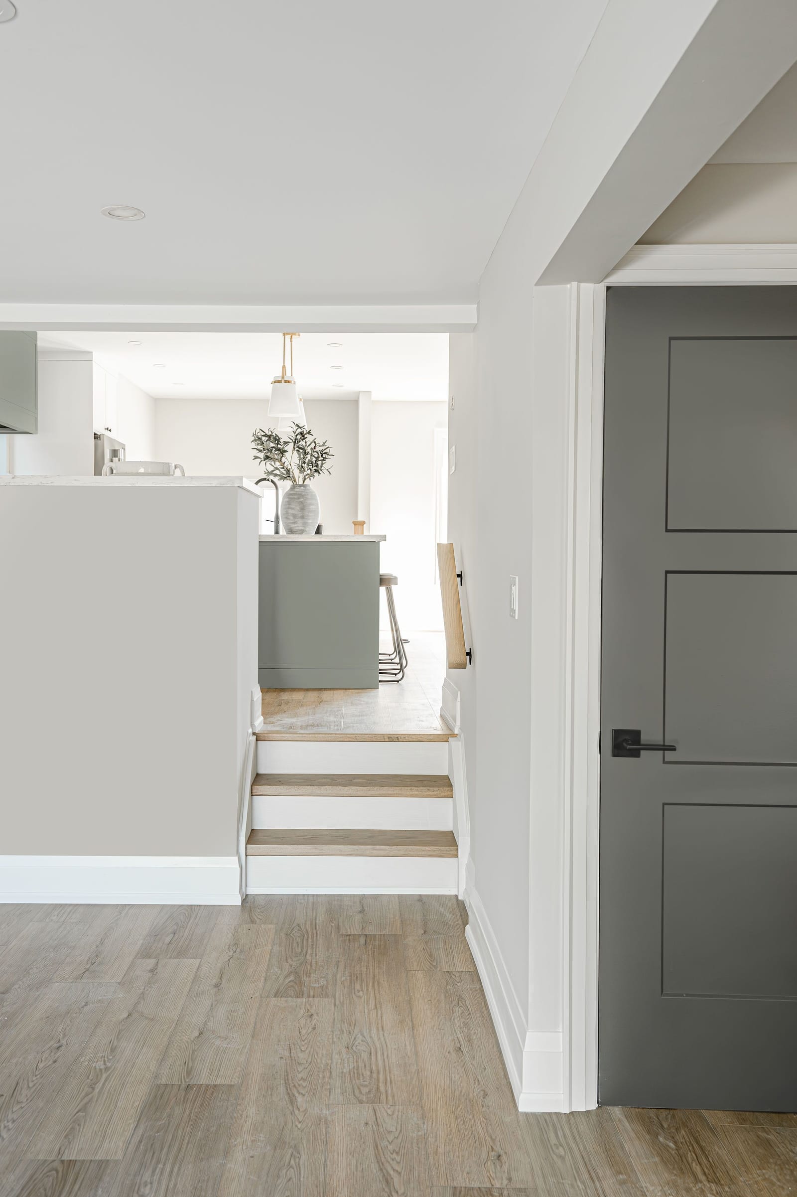 A short run of oak steps between levels, looking up into the kitchen past a dark grey panelled door