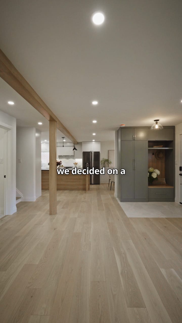 The opened-up Bellamy main floor: wide oak plank floor, a wrapped post and beam, and a sage-green storage wall by the front door
