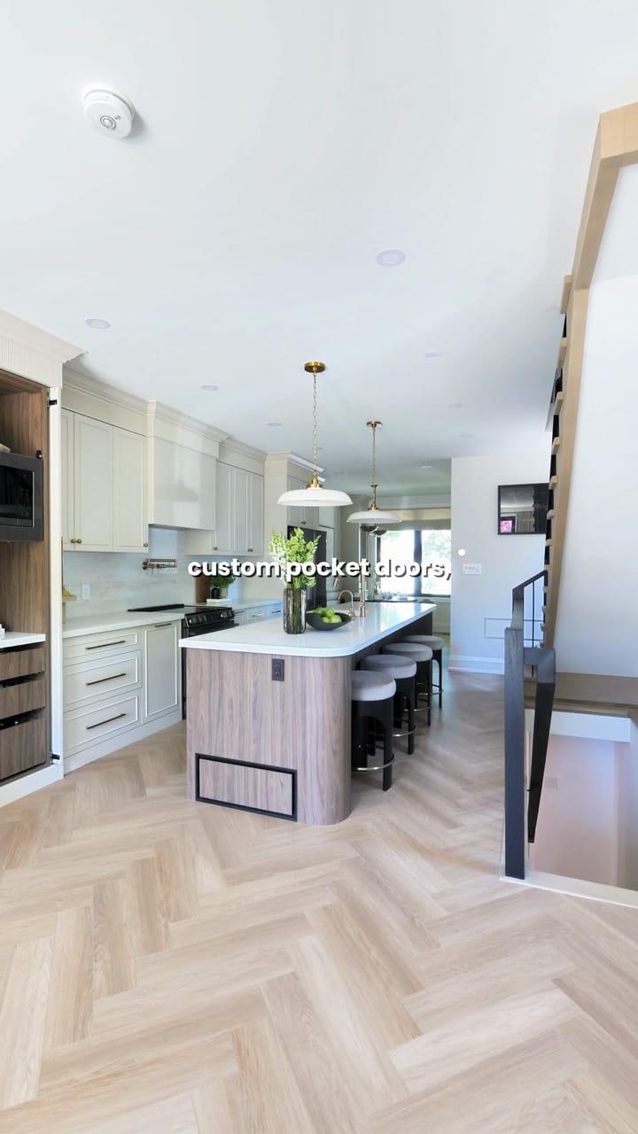 A long kitchen with a walnut island, cream cabinets and a herringbone floor running toward the rear windows
