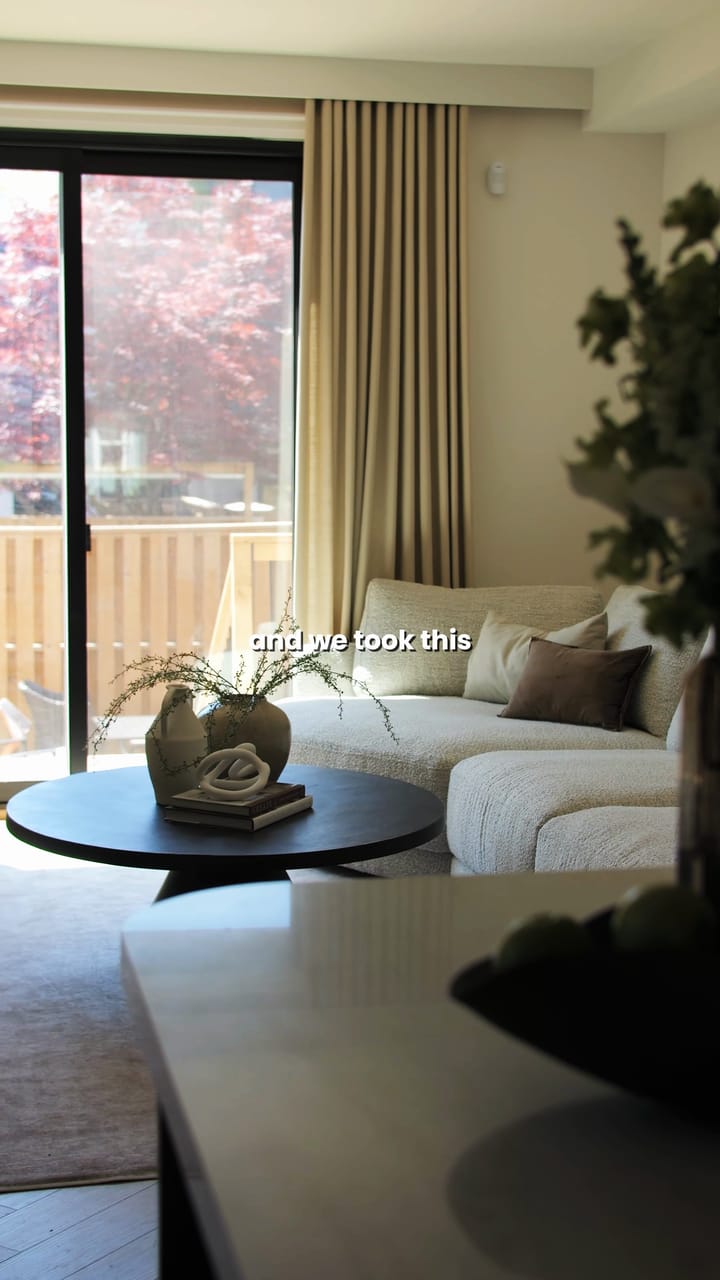 A living room with a cream sectional sofa, a round black coffee table and a sliding door to a wooden deck