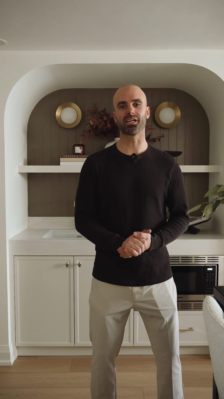 James Jarvis in the finished basement, standing in front of a curved kitchenette alcove with brass sconces, white cabinets and a built-in microwave